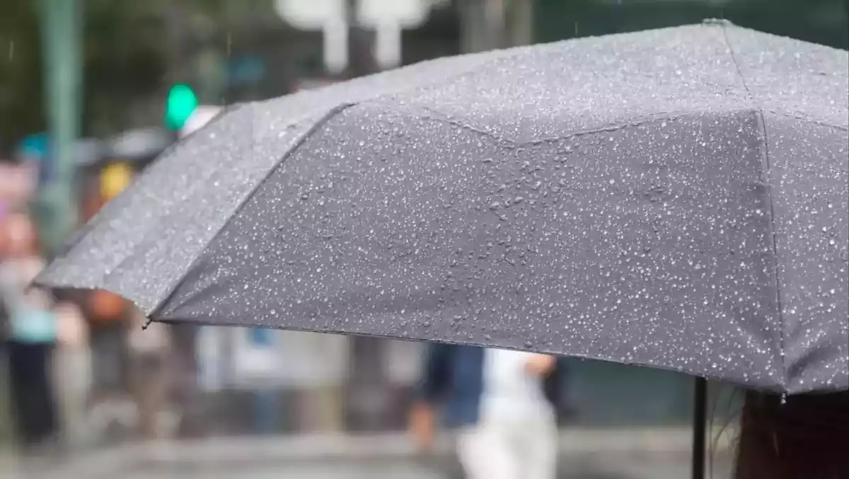 Una persona en primer pla sota un paraigua amb pluja caient.